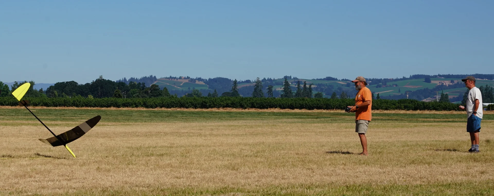 Two PASS pilots watching a perfect landing at St. Paul field — Oregon hills behind them